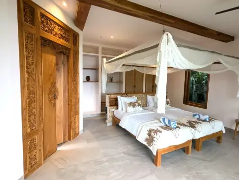 A bright tropical bedroom featuring two twin beds with white canopies and a large hand-carved wooden door.