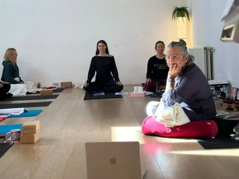 A meditation instructor leads a session for in-person students and a remote audience via laptop.