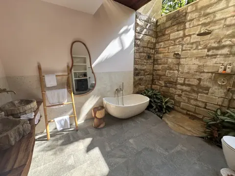 An open-air luxury bathroom with a white soaking tub, stone walls, and wooden accents.