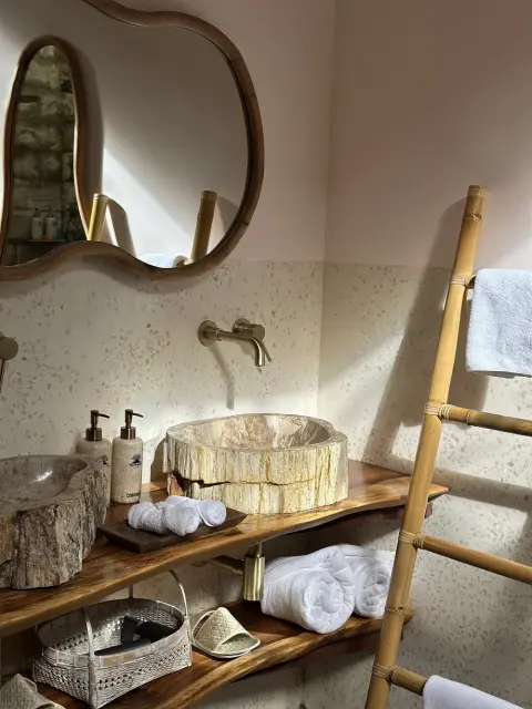 A petrified wood vessel sink on a live-edge wooden vanity with gold fixtures.