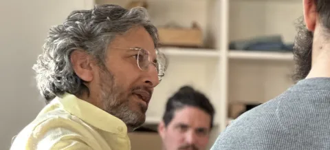 Yoga scientist Sanjeev Bhanot leading a coaching session in a bright studio with wooden shelves.