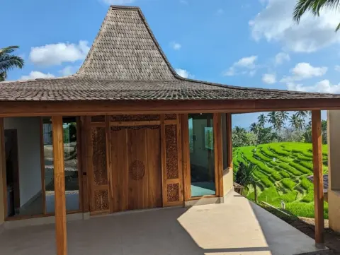 Traditional wooden Joglo villa at Puri Dajuma Terrace overlooking lush green rice terraces in Bali.