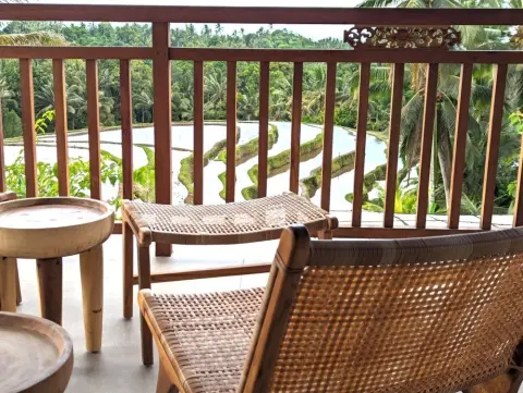 Wooden balcony furniture overlooking lush green rice terraces and palm trees.